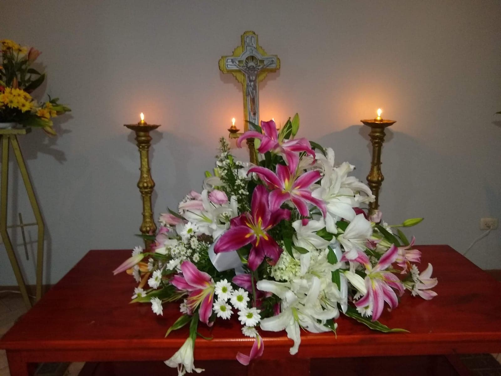 Arreglo floral junto a la cruz y las velas del altar