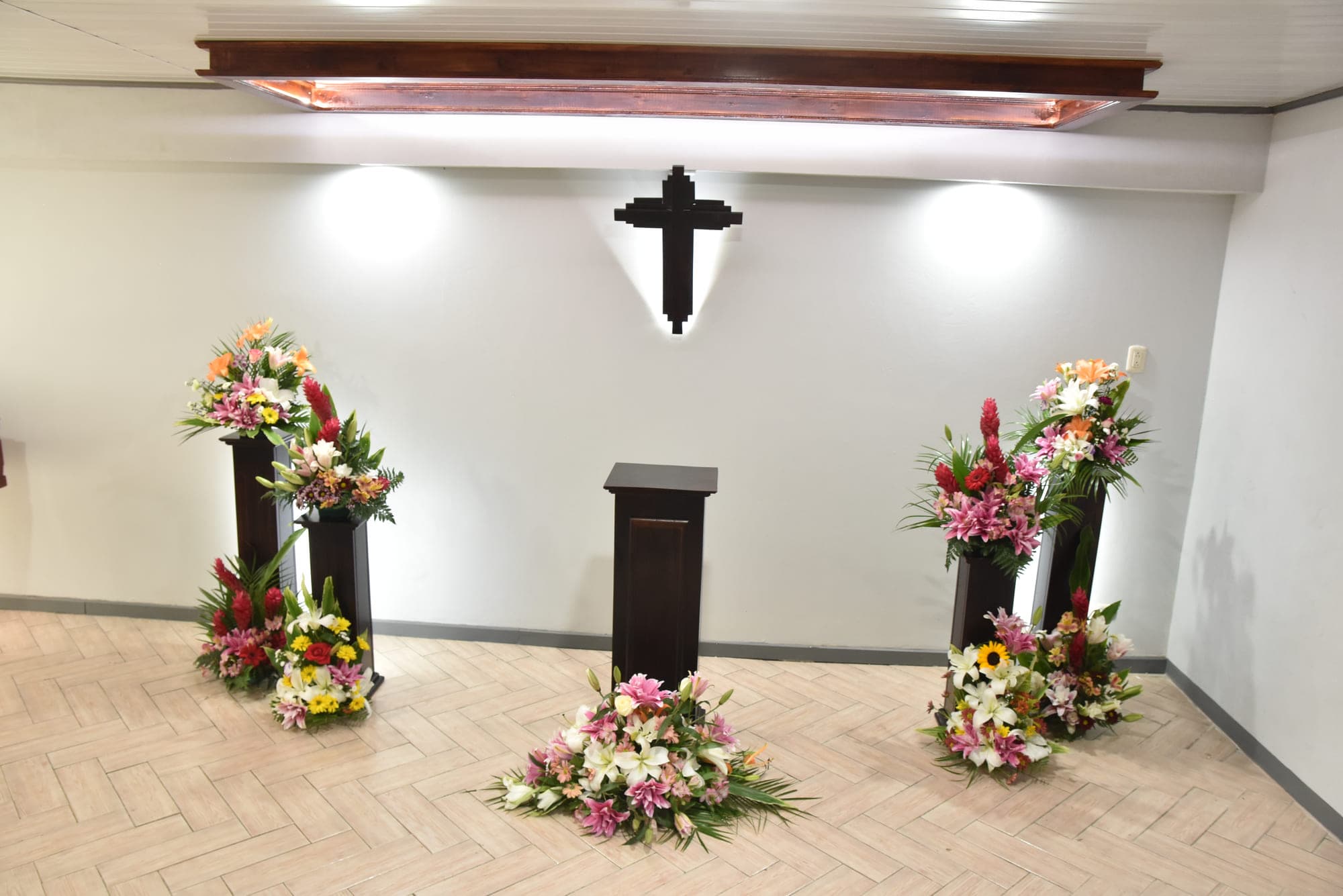 Sala de velación con la cruz iluminada y arreglos florales a ambos lados